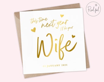 May include: A white card with gold foil lettering that reads "This time next year I'll be your Wife" with a date of January 12, 2021.