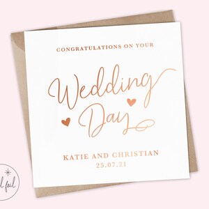 K&ouml;nnte beinhalten: Eine wei&szlig;e Karte mit einem ros&eacute;goldenen Foliendesign, auf der "Herzlichen Gl&uuml;ckwunsch zu Ihrem Hochzeitstag" mit zwei kleinen Herzen steht. Die Karte enth&auml;lt auch die Namen "Katie und Christian" und das Datum "25.07.21".