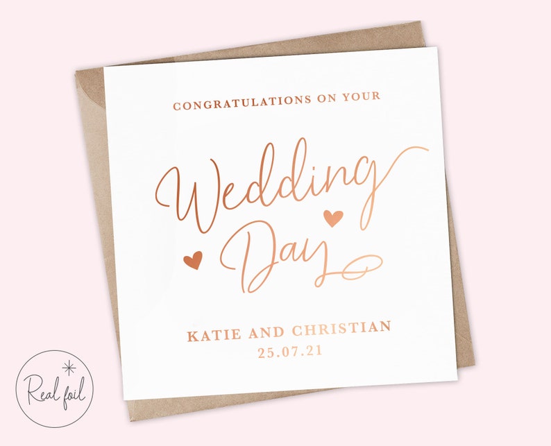 K&ouml;nnte beinhalten: Eine wei&szlig;e Karte mit einem ros&eacute;goldenen Foliendesign, auf der "Herzlichen Gl&uuml;ckwunsch zu Ihrem Hochzeitstag" mit zwei kleinen Herzen steht. Die Karte enth&auml;lt auch die Namen "Katie und Christian" und das Datum "25.07.21".