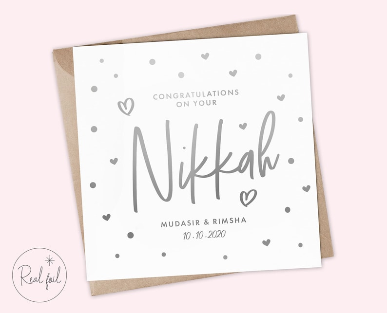 May include: A white card with silver foil lettering that says "Congratulations on your Nikkah. Mudasir & Rimsha 10.10.2020". The card is decorated with silver foil hearts and dots.