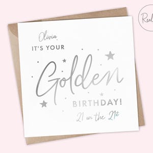 May include: A white card with silver foil lettering that says "Olivia, It's your Golden Birthday! 21 on the 21st".