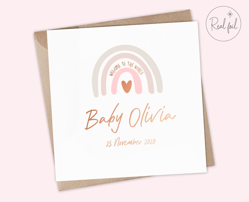 Puede incluir: Una tarjeta blanca con un arco&iacute;ris rosa y beige con un coraz&oacute;n rosa en el centro. El texto "Bienvenido al mundo" est&aacute; escrito en el arco&iacute;ris. Debajo del arco&iacute;ris est&aacute; el texto "Baby Olivia" en color cobre y la fecha "23 de noviembre de 2020".