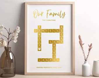 May include: A framed family name art print with gold lettering on a white background. The words "Our Family" are at the top, with the family name below. The names of family members are spelled out in a crossword-style design. The phrase "MAKING MEMORIES SINCE 2019" is at the bottom.