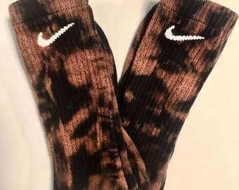 May include: A pair of black and brown tie-dye socks with a white Nike swoosh logo on each sock.