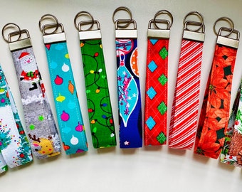 May include: A collection of fabric keychains with various holiday-themed patterns. Designs include Christmas trees, snowflakes, Santa Claus, ornaments, candy canes, and Thanksgiving motifs. Each keychain has a silver-colored metal clasp.