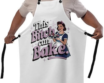 Puede incluir: Delantal blanco con correas negras con el texto "This Bitch can Bake" en una fuente retro. El delantal tiene un gráfico de una mujer sosteniendo una bandeja de productos horneados. El delantal es usado por una persona.
