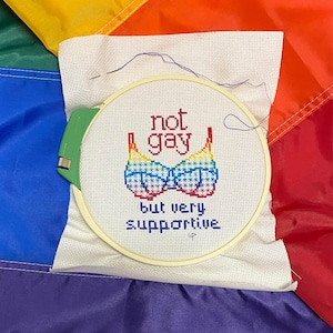 Peut inclure: Un cercle de broderie blanc avec un motif de soutien-gorge arc-en-ciel et le texte "not gay but very supportive".