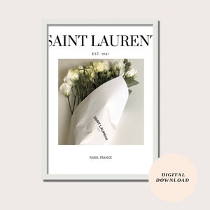 May include: A white framed print with the text "SAINT LAURENT" in black, "EST. 1961" in smaller black text, and "PARIS, FRANCE" in black text. The print features a photo of a bouquet of white flowers wrapped in white paper with the "SAINT LAURENT" logo printed on the paper.