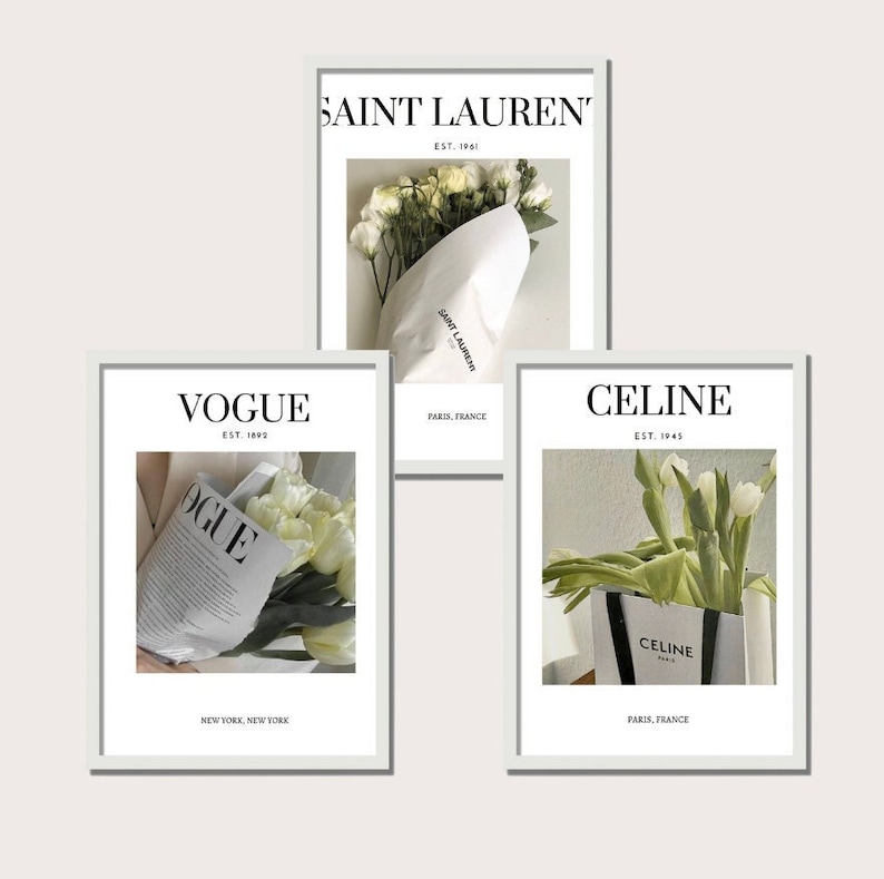 May include: Three framed prints with white flowers and text. The top print features the text "SAINT LAUREN' EST. 1961" and a bouquet of white flowers wrapped in white paper. The middle print features the text "VOGUE EST. 1892" and a bouquet of white flowers wrapped in a newspaper with the word "OGUE" visible. The bottom print features the text "CELINE EST. 1945" and a bouquet of white flowers wrapped in a white bag with the text "CELINE PARIS" visible.