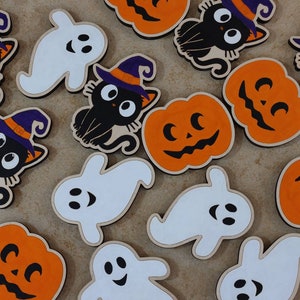 May include: A collection of Halloween-themed wooden ornaments featuring pumpkins, ghosts, and black cats. The ornaments are painted in orange, white, and black.