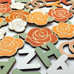 May include: Wooden craft supplies featuring orange and white roses, green leaves, and letters in white, green, and brown. The letters spell out the word "ZACHARY".