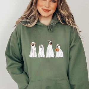 May include: A green hooded sweatshirt featuring a graphic of four dogs dressed as ghosts. The dogs are wearing white sheets with their heads poking out. One dog is holding a pumpkin.