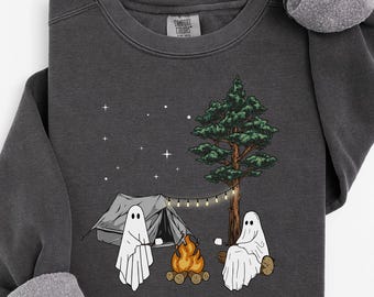 May include: Dark gray sweatshirt with a camping scene featuring two ghosts, a tent, a campfire, and a tree. The design includes string lights and stars. The sweatshirt has a crew neck and long sleeves with rolled cuffs.