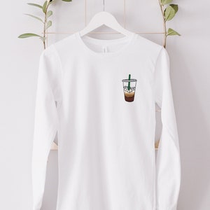 Peut inclure: T-shirt &agrave; manches longues blanc avec un graphique d'un caf&eacute; glac&eacute; sur le devant.