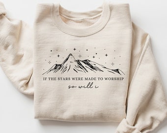 Puede incluir: Una sudadera beige con un gráfico negro de montañas y estrellas y el texto "Si las estrellas fueron hechas para adorar, yo también lo haré".