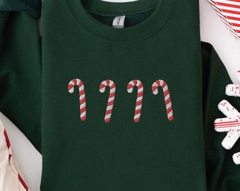 May include: A dark green sweatshirt with a festive design of four red and white candy canes. The sweatshirt is laid flat on a white surface.