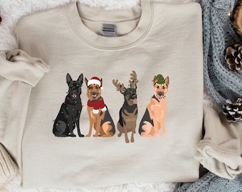 May include: A beige sweatshirt with a graphic of four black German Shepherd dogs wearing Christmas hats and accessories. The dogs are wearing Santa hats, reindeer antlers, and a green elf hat.