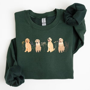 May include: A dark green sweatshirt with a graphic of four golden retriever dogs sitting in a row with flowers. The dogs are all facing forward and have their tongues sticking out. The flowers are in shades of pink, purple, and yellow.