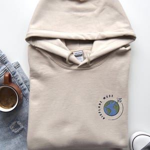 May include: A beige hoodie with a graphic of a globe and airplane with the text "Airplane Mode" on the front.