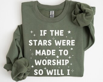 Puede incluir: Una sudadera verde con texto blanco que dice "Si las estrellas fueron hechas para adorar, yo también lo haré." El texto está rodeado de pequeñas estrellas. La sudadera tiene una manga enrollada.