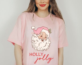 May include: Pink t-shirt featuring a cartoon Santa Claus graphic and the text "HOLLY jolly" in red.