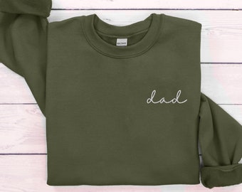 Puede incluir: Una sudadera verde oscuro con la palabra "dad" bordada en la parte delantera en cursiva blanca.