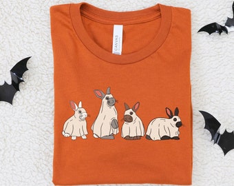 Könnte beinhalten: Orangefarbenes T-Shirt mit einem Aufdruck von vier weißen Kaninchen, die als Geister verkleidet sind. Die Kaninchen tragen weiße Laken mit Augenlöchern. Der Text "EMMA & ANNA" ist unter dem Aufdruck gedruckt.