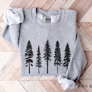May include: Gray sweatshirt with a black silhouette of five pine trees printed on the front. The sweatshirt has a crew neck and long sleeves.