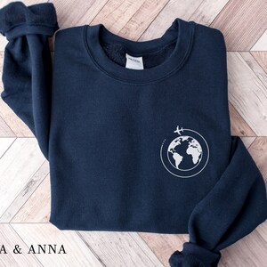 May include: A navy blue sweatshirt with a white graphic of a globe with airplanes flying around it.