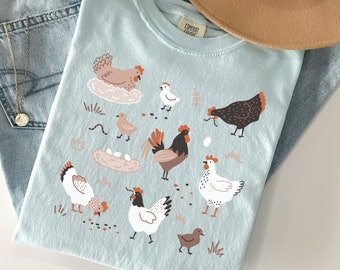 May include: A light blue t-shirt with a graphic print of chickens and eggs. The text "Comfort Colors" is visible on the shirt.