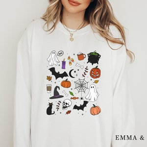 May include: White sweatshirt with a black and white illustration of various Halloween themed items including a ghost, a bat, a witch's hat, a pumpkin, a cauldron, a spider web, and a skull.