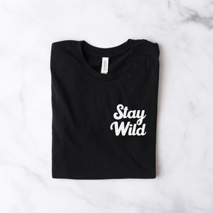 May include: Black t-shirt with white text that says "Stay Wild" in a retro font.