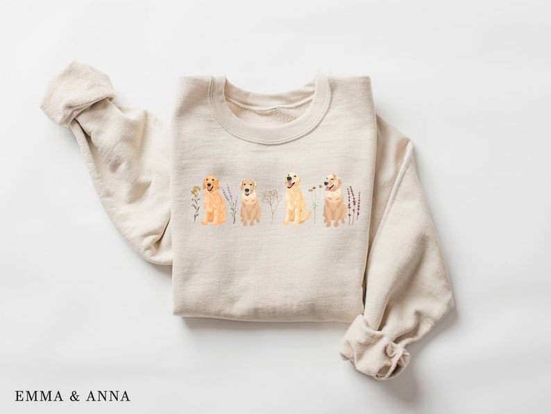 May include: A beige sweatshirt with a graphic of four golden retriever dogs sitting in a row with wildflowers behind them.
