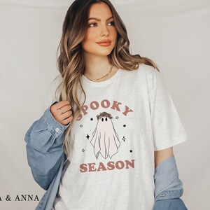 May include: A white t-shirt with a pink ghost wearing a floral crown and the text "Spooky Season".