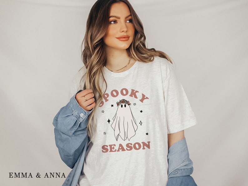 May include: A white t-shirt with a pink ghost wearing a floral crown and the text "Spooky Season".