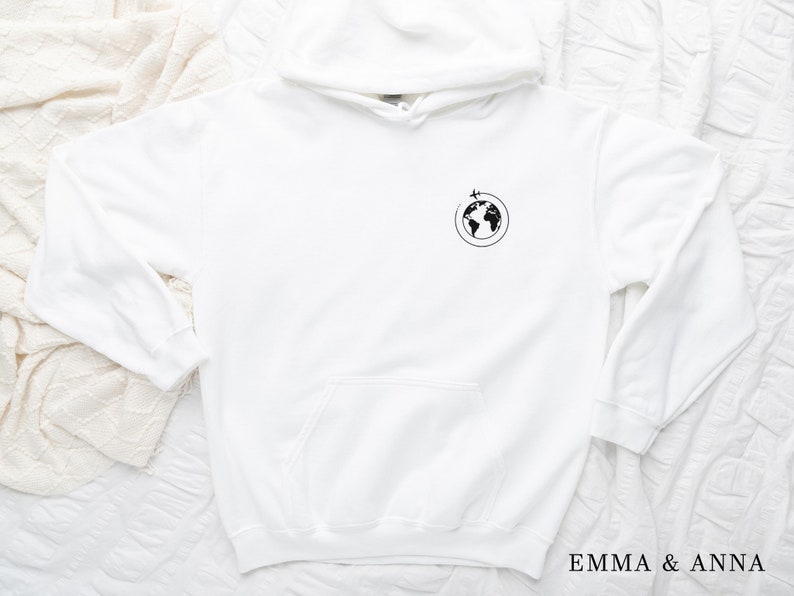 May include: White hoodie with a black graphic of a globe with a plane flying around it. The text "EMMA & ANNA" is printed on the bottom right corner of the image.