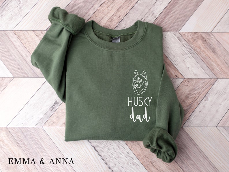 Pode incluir: Uma camisa de moletom verde com um contorno branco de um c&atilde;o husky e o texto "HUSKY dad" na frente.