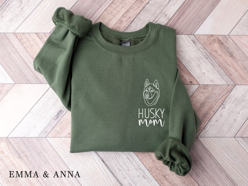 Pode incluir: Uma camisa de moletom verde com um contorno branco de um c&atilde;o husky e o texto "HUSKY MOM" na frente.