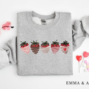 Puede incluir: Sudadera gris con un gr&aacute;fico de cinco fresas cubiertas de chocolate con un chorrito blanco. Las fresas est&aacute;n dispuestas en una fila a trav&eacute;s del centro de la sudadera.