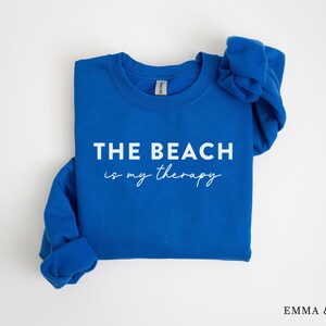 以下が含まれることがあります： ロイヤルブルーのトレーナーに、白い文字で「THE BEACH is my therapy」と書かれています。