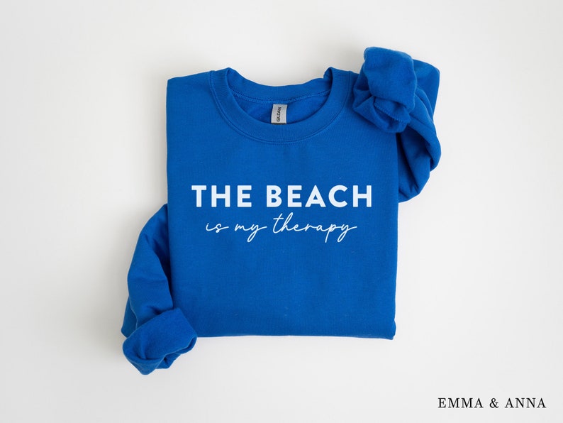 以下が含まれることがあります： ロイヤルブルーのトレーナーに、白い文字で「THE BEACH is my therapy」と書かれています。