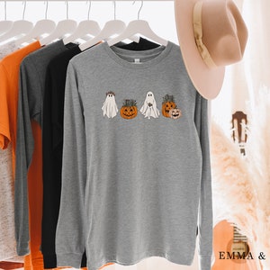 May include: A gray long-sleeve shirt with a graphic of three ghosts holding pumpkins. The ghosts are wearing floral crowns and the pumpkins have green stems.