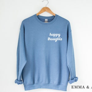 May include: A light blue sweatshirt with the text "happy thoughts" printed in white on the front.
