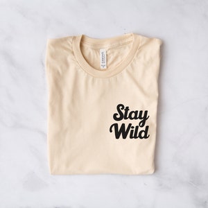 May include: A folded beige t-shirt with a black graphic that says "Stay Wild" on the front.