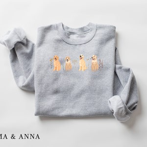 May include: Gray sweatshirt with a print of four golden retriever dogs sitting in a row with flowers and grass behind them.