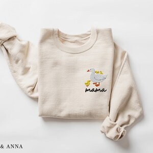 May include: A beige sweatshirt with an embroidered design of a goose with goslings. The text "mama" is embroidered below the goose.