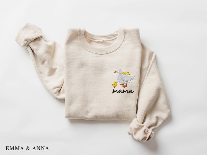 May include: A beige sweatshirt with an embroidered design of a goose with goslings. The text "mama" is embroidered below the goose.