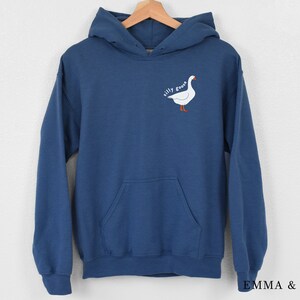K&ouml;nnte beinhalten: Ein dunkelblauer Kapuzenpullover mit einem wei&szlig;en G&auml;nse-Motiv und dem Text "silly goose" auf der Vorderseite.