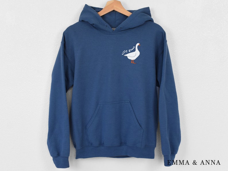 K&ouml;nnte beinhalten: Ein dunkelblauer Kapuzenpullover mit einem wei&szlig;en G&auml;nse-Motiv und dem Text "silly goose" auf der Vorderseite.