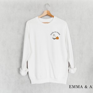 May include: White sweatshirt with long sleeves and a crew neck. The sweatshirt has a small embroidered design on the front that says "trick or treat" with a ghost and a pumpkin.